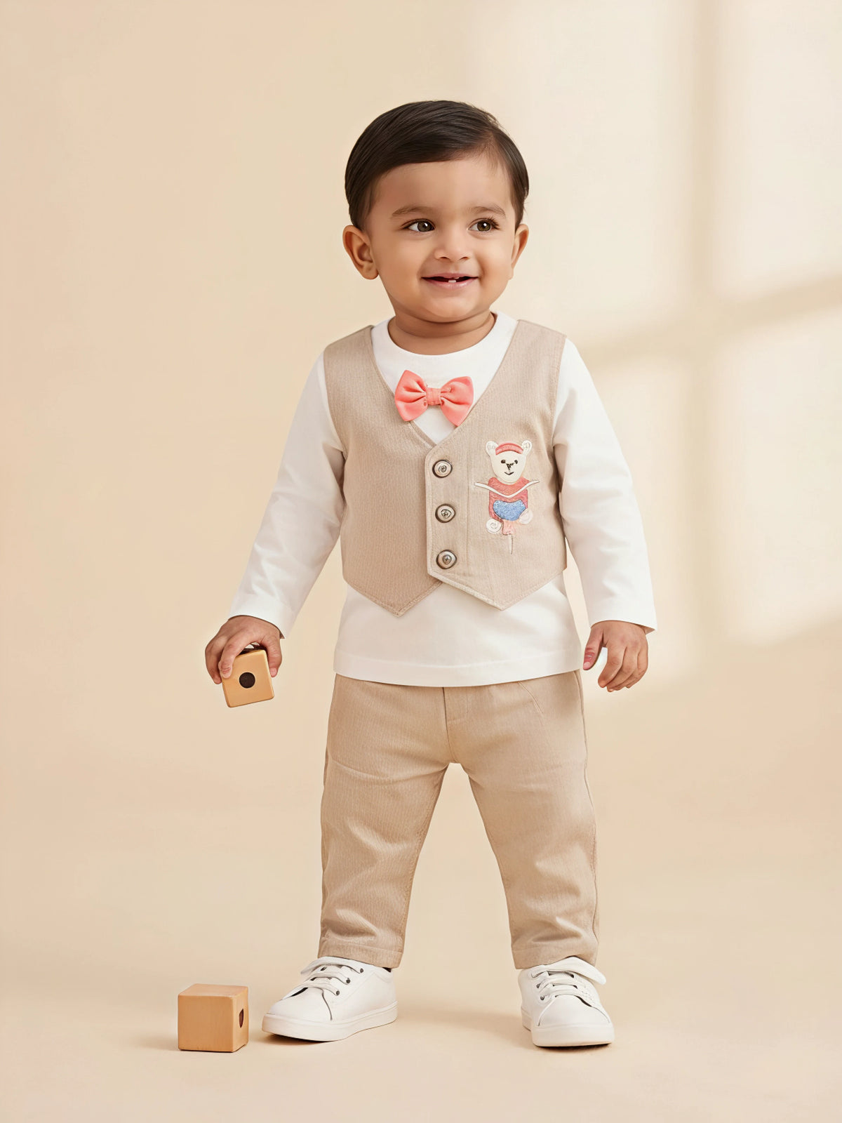 Boys cream clothing set featuring a sleeveless waistcoat with a teddy bear embroidery, long sleeve top with a bow tie, and cream trousers.