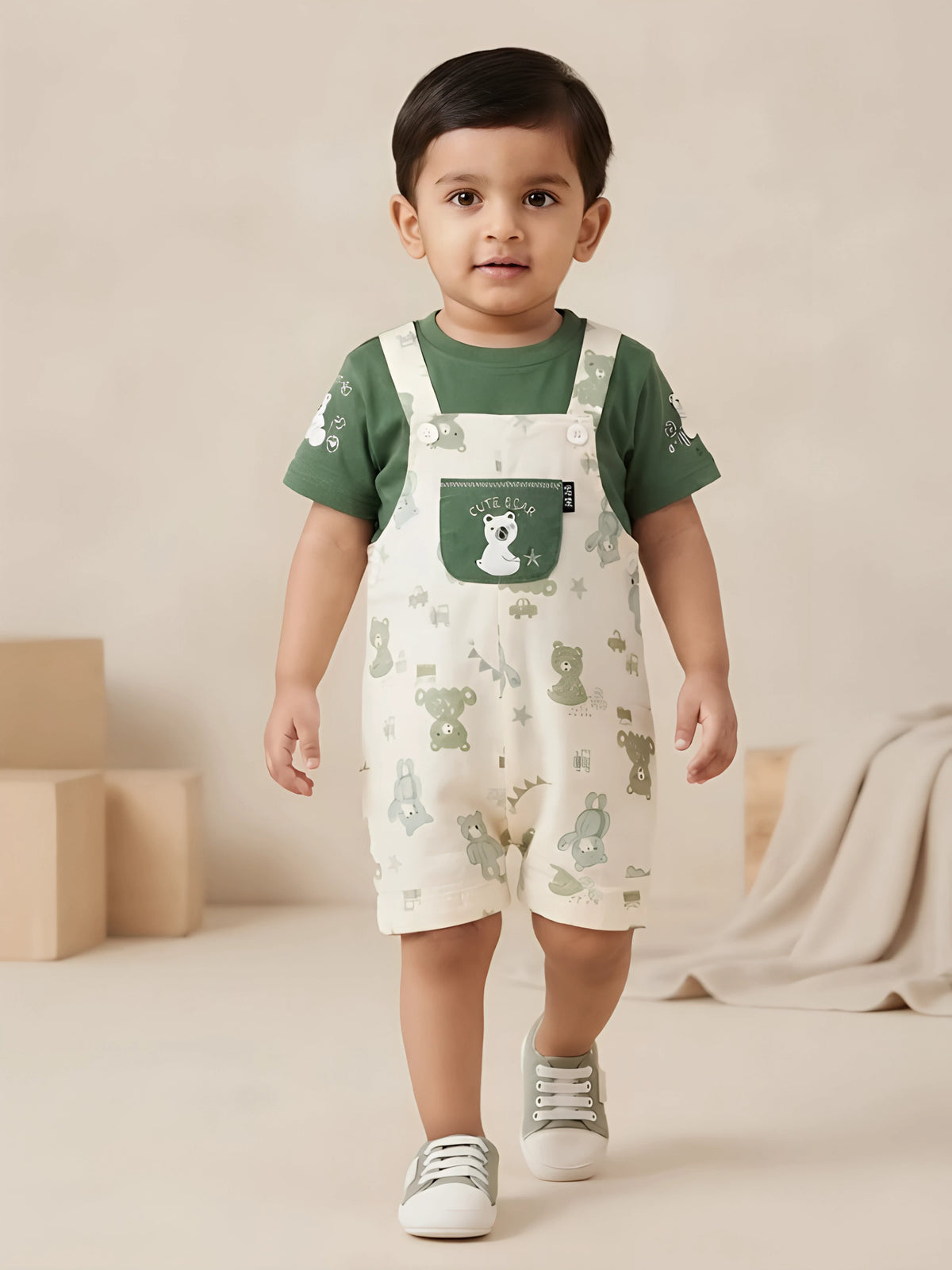 Infant boy wearing a green short-sleeve t-shirt and printed teddy bear dungaree shorts with a front patch pocket.