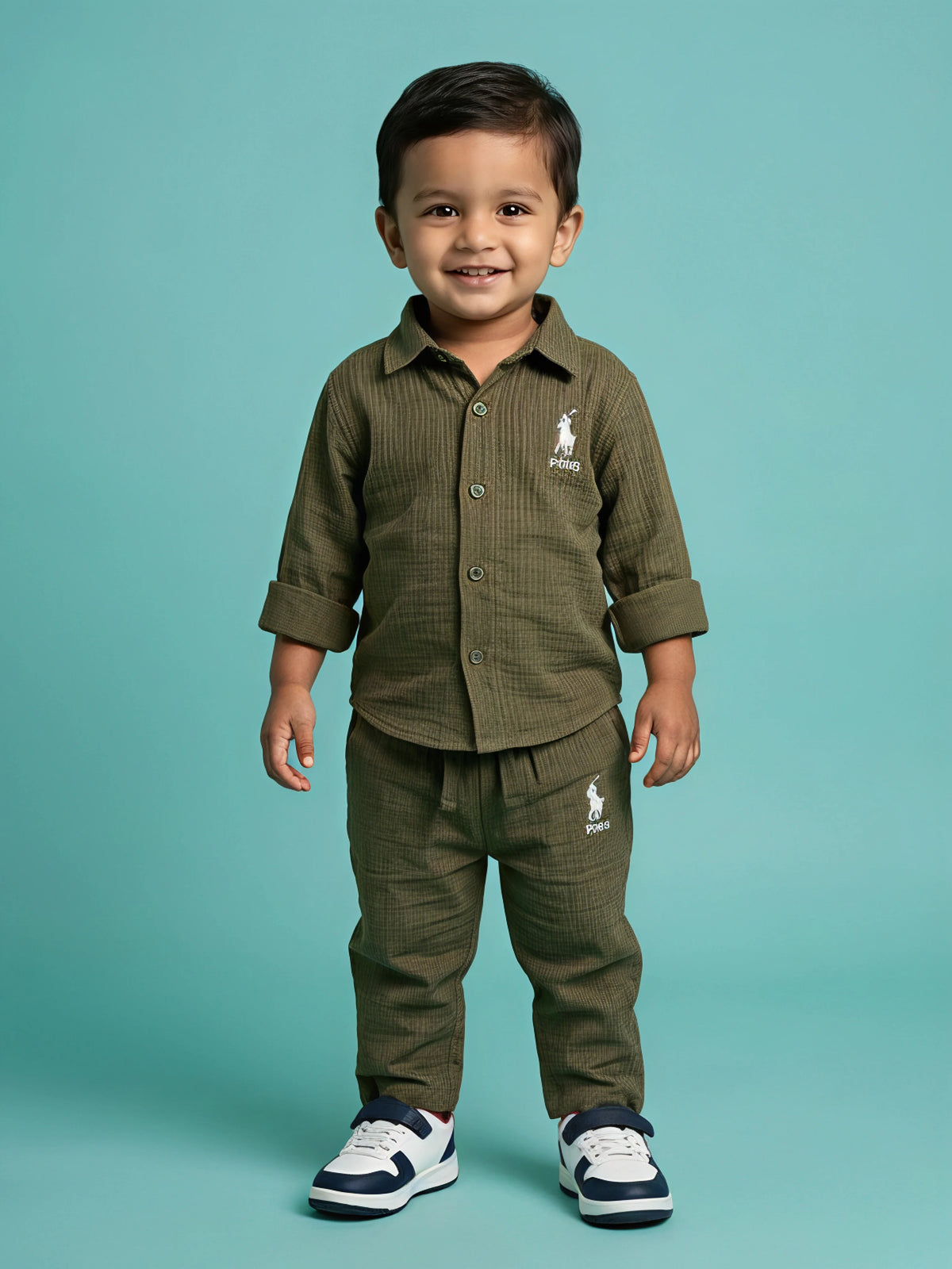 Young boy wearing an olive green textured shirt and matching trouser co-ord set with white sneakers