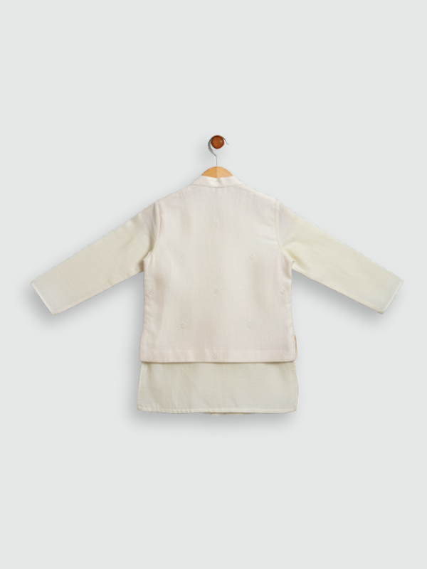 A young boy standing and smiling, wearing a cream/off-white long-sleeved kurta and pajama set with beautiful, detailed multi-color bird and floral embroidery across the chest.