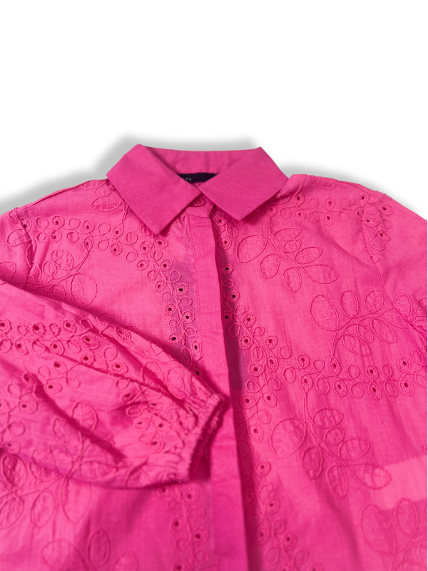 Front view of a girls' bright hot pink long-sleeve button-up blouse completely covered in delicate white eyelet (broderie anglaise) embroidery, hanging on a wooden hanger.