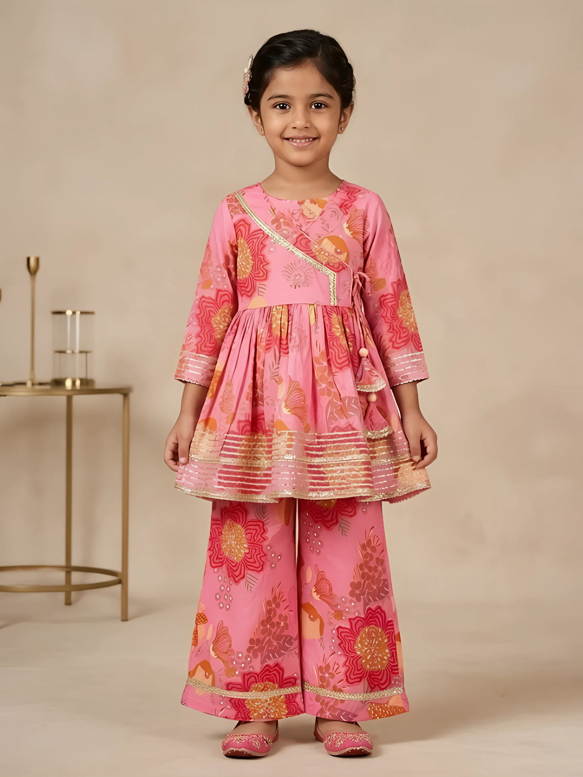 Young girl wearing a pink floral printed Angrakha style peplum kurti with flared sharara bottoms and gold lace trimming