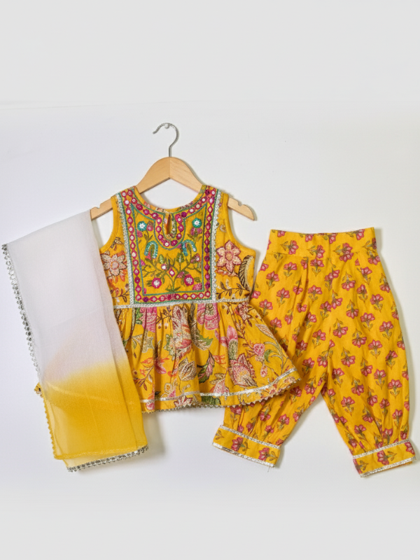 Front view of a girls' sleeveless yellow peplum top with all-over pink/green floral print and a heavily embroidered neckline and yoke, hanging on a wooden hanger.