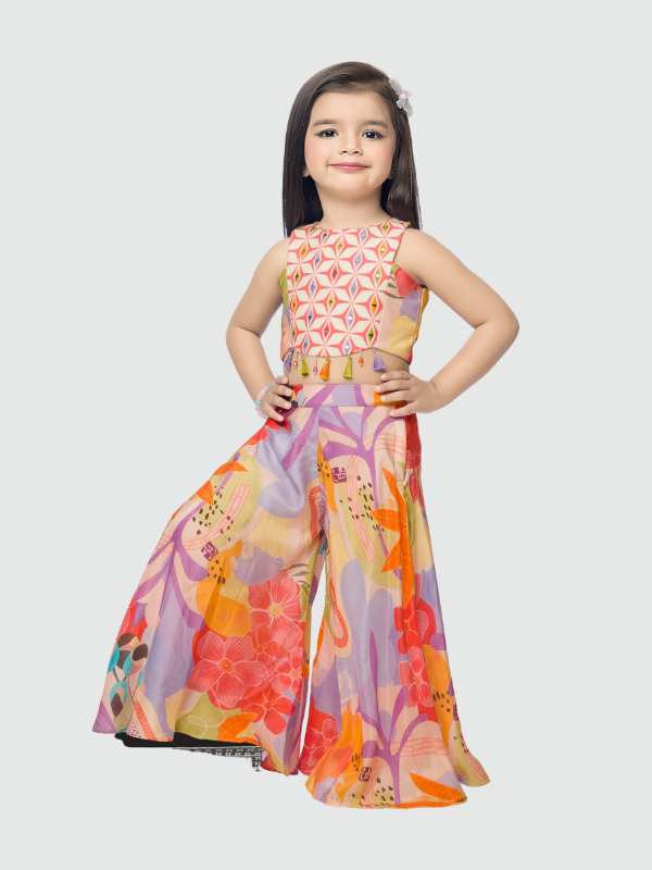 Young girl smiling in a sleeveless multi-color ethnic set featuring a geometric print crop top with tassels and wide-leg lavender palazzo pants with an abstract tropical floral print.