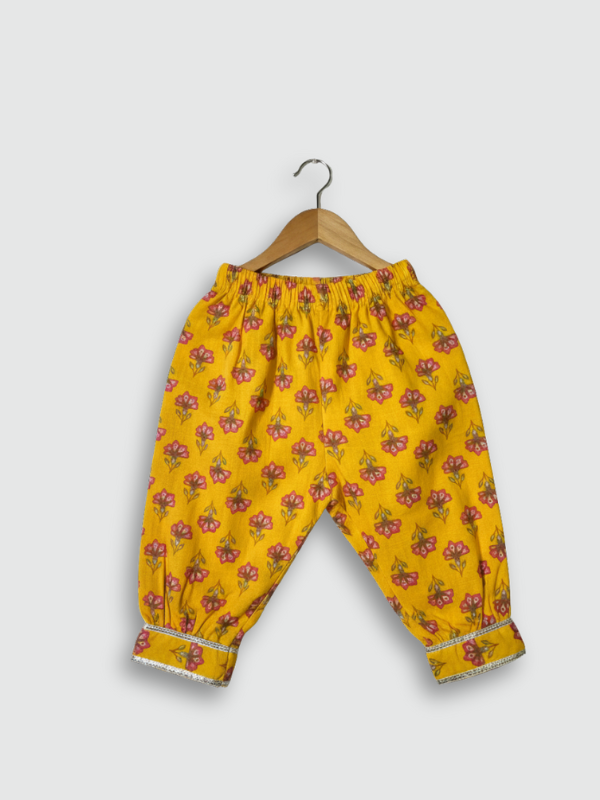 Front view of a girls' sleeveless yellow peplum top with all-over pink/green floral print and a heavily embroidered neckline and yoke, hanging on a wooden hanger.