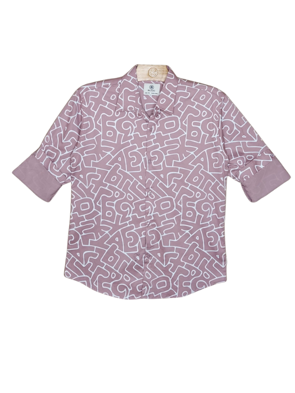 Young boy smiling in a cream/off-white collared shirt with small, whimsical adventure-themed embroideries, paired with dark brown/olive slim-fit trousers and white sneakers.