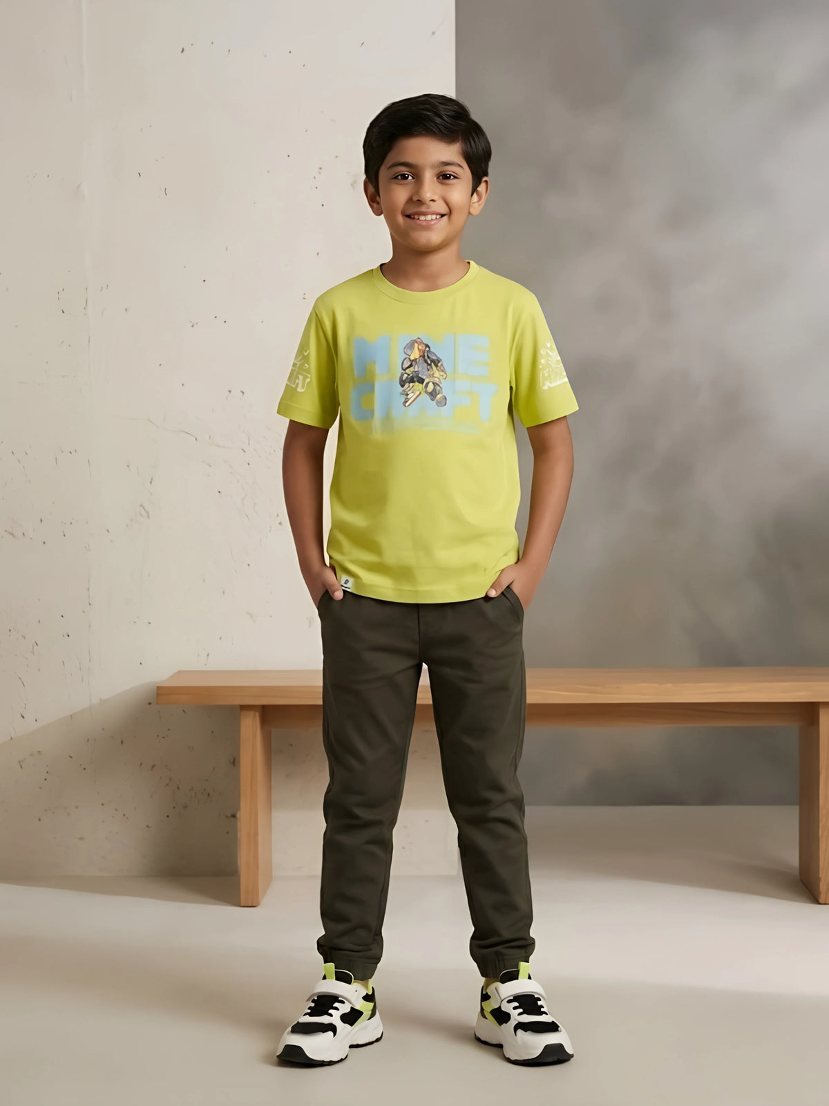Young boy wearing a vibrant lime green short-sleeve casual graphic t-shirt paired with olive green trousers and sneakers.