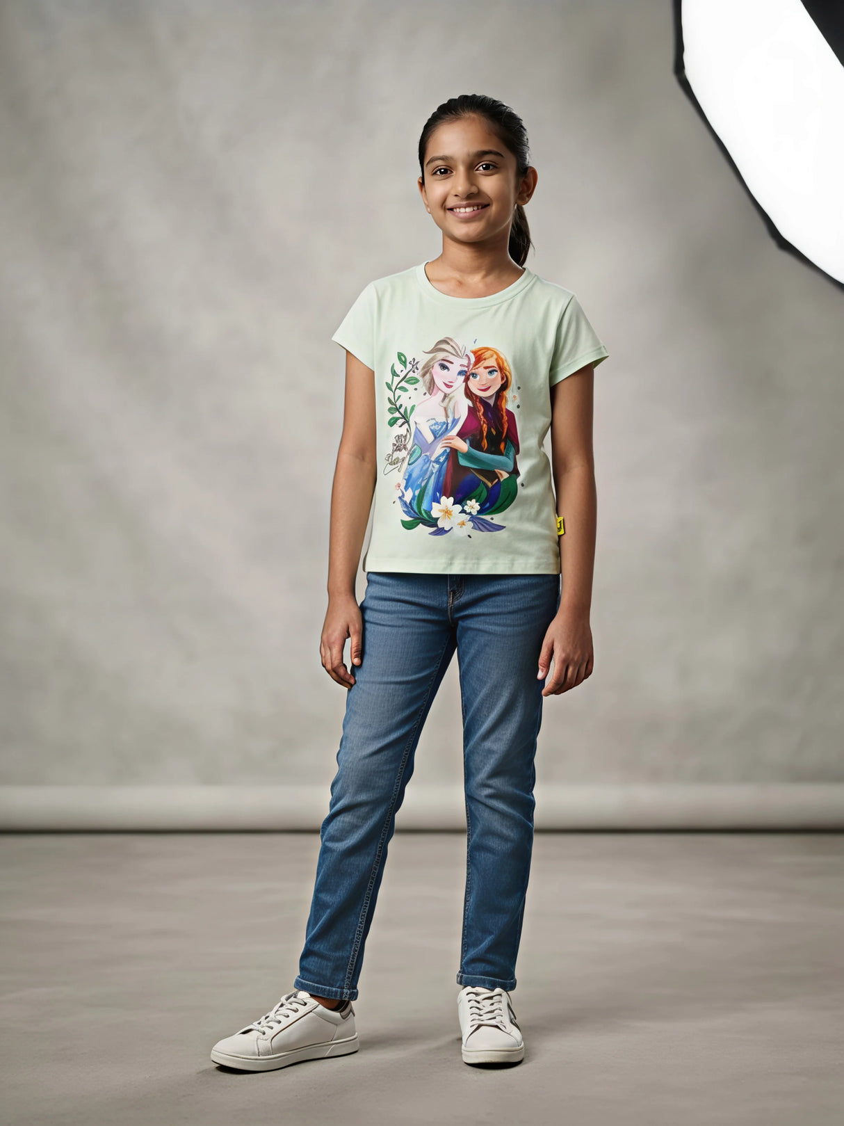 Young girl wearing a light green short-sleeve Disney Frozen graphic t-shirt with Elsa and Anna print paired with blue jeans