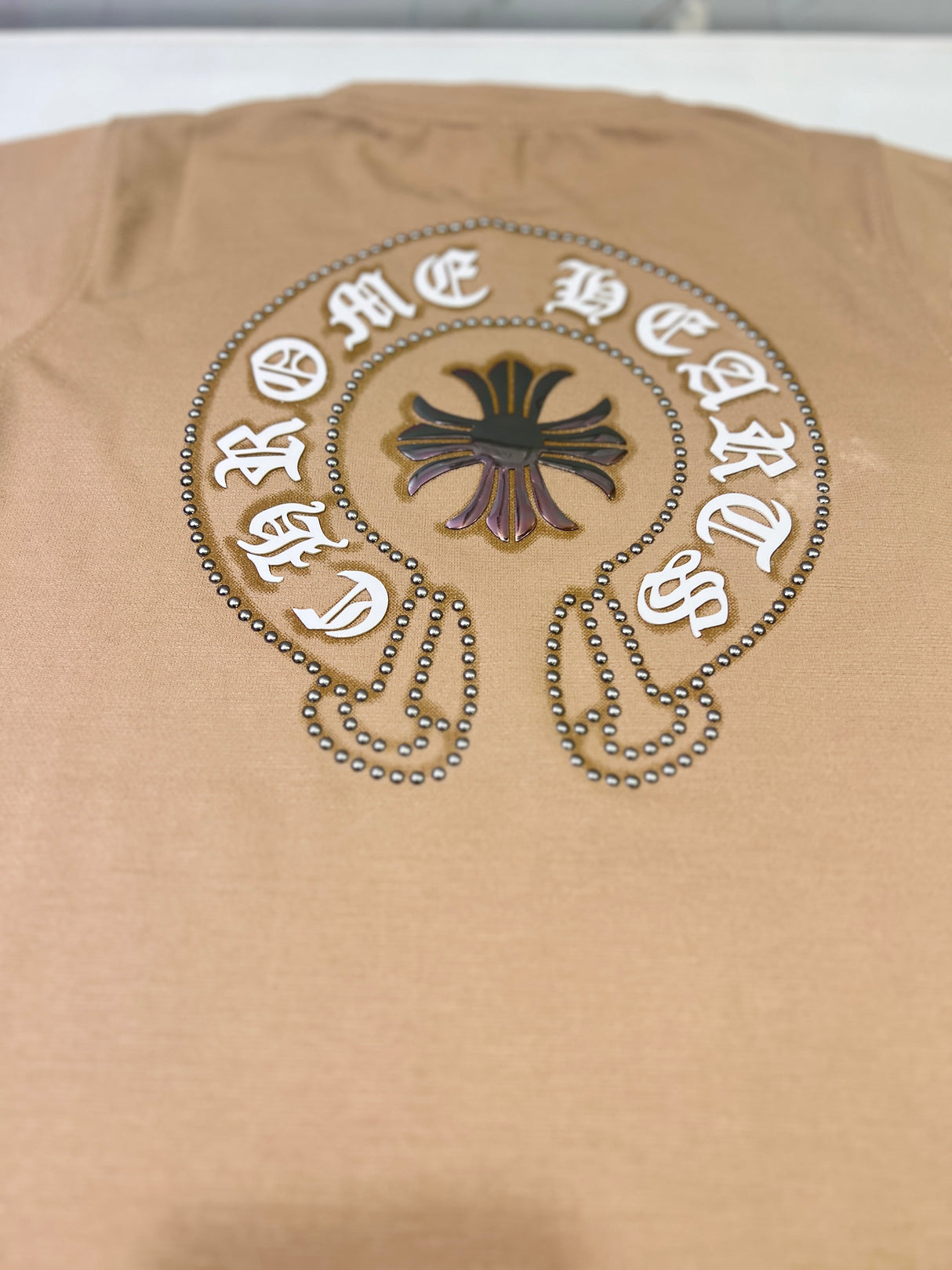 Tan/Brown boys' short-sleeve T-shirt with a small circular distressed cross and text logo graphic on the left chest, hanging on a white background.