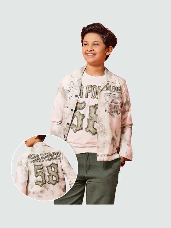 Smiling boy wearing a white/grey distressed shacket (shirt-jacket) with 'Air Force' text and a bold '58' graphic on the back, layered over a white printed tee, and paired with green check trousers.