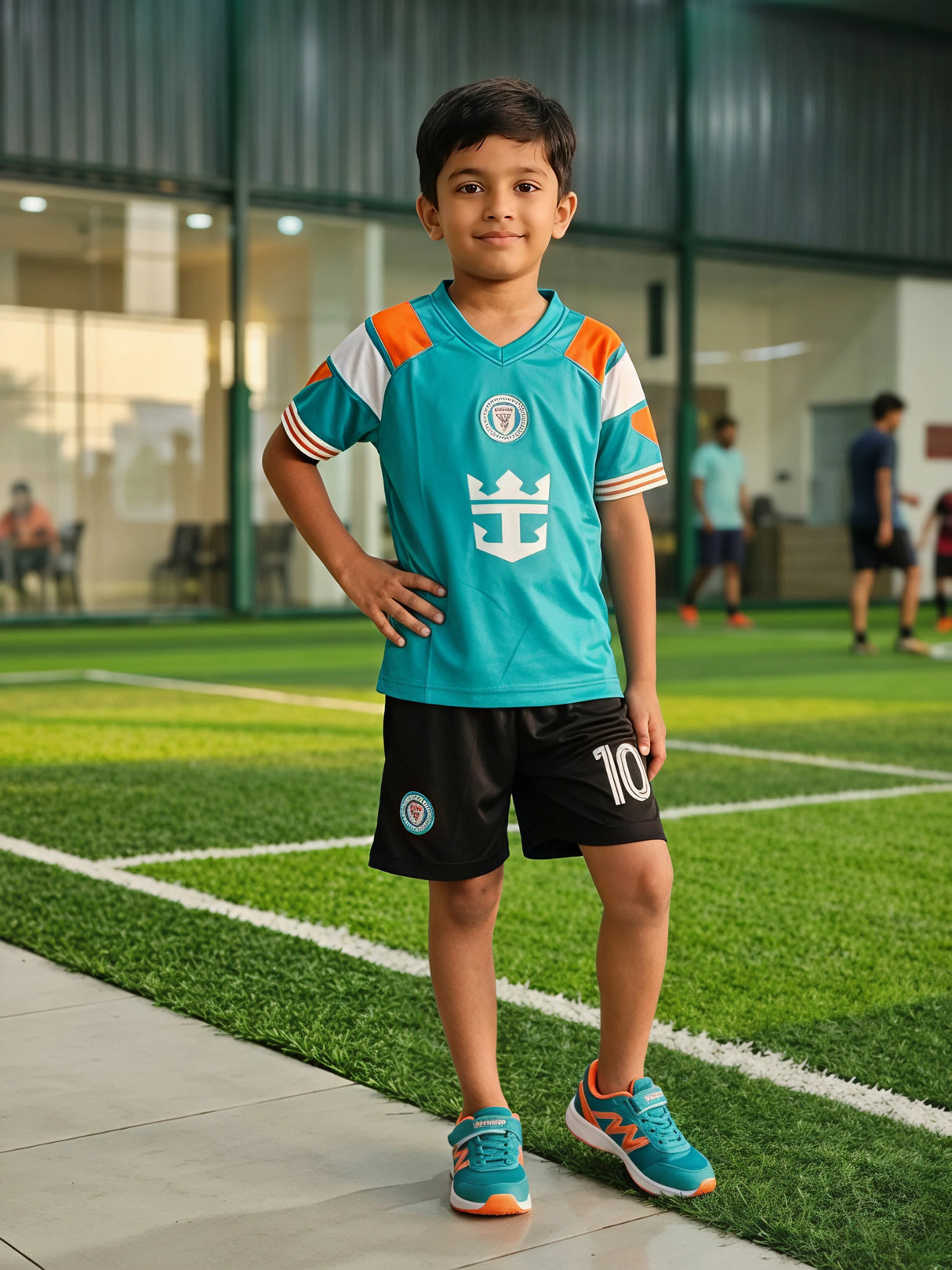 A young boy posing on a football turf field wearing a teal green and orange athletic jersey with matching black sports shorts printed with number 10.