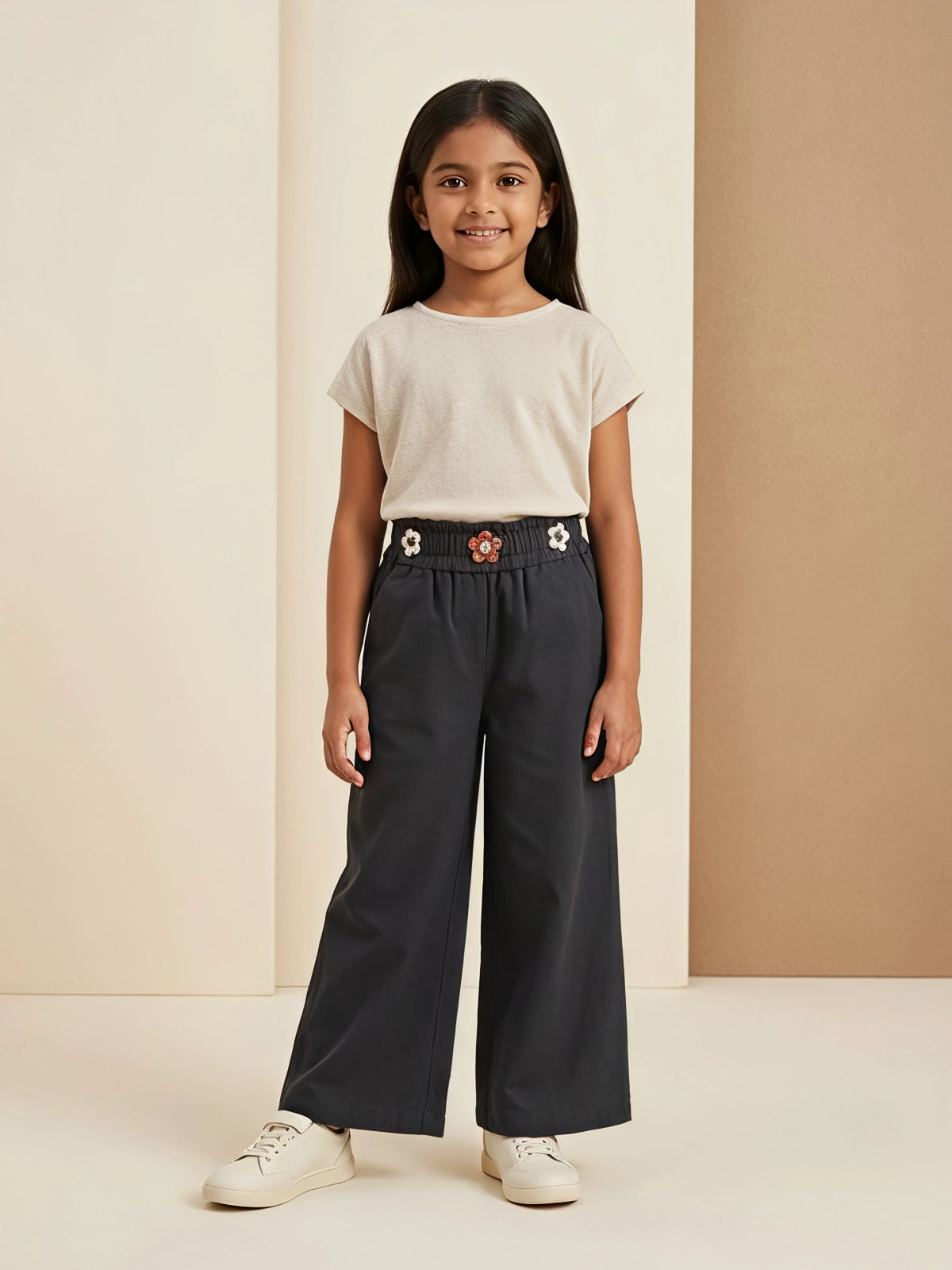 Young girl wearing black wide-leg casual pants with floral embellishments on the waistband and a plain beige t-shirt