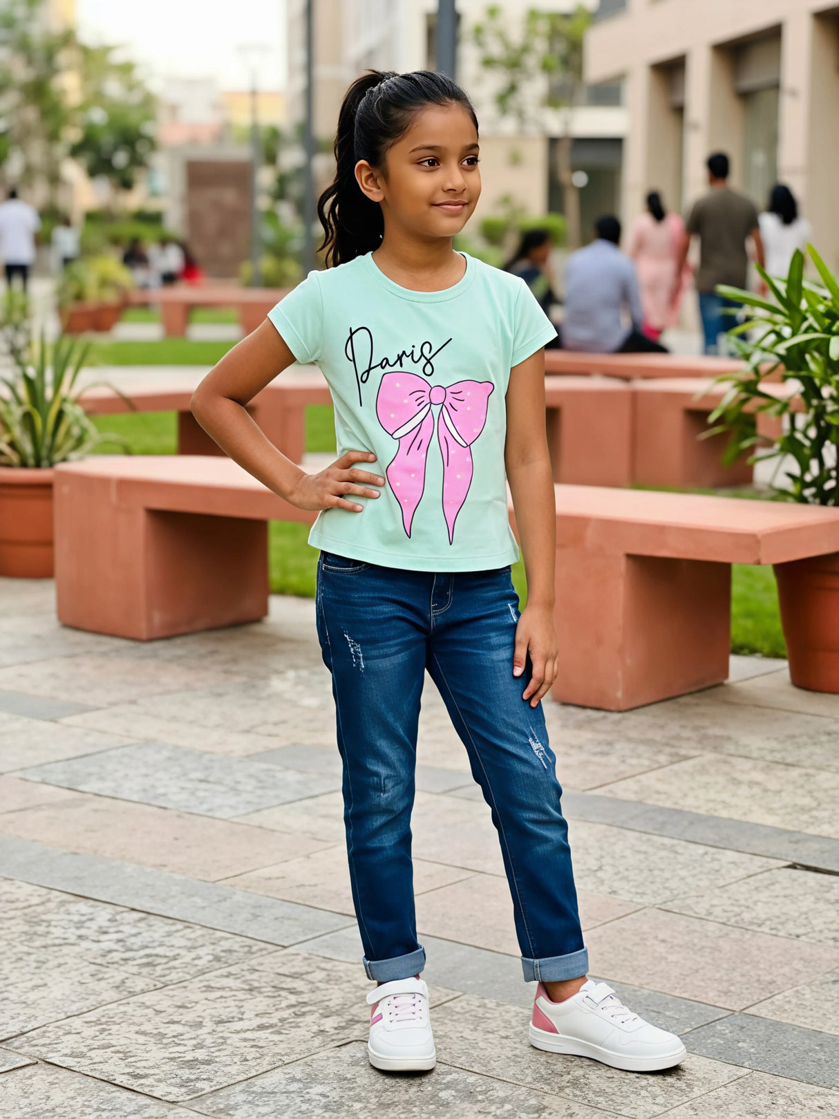 A young girl wearing a mint green short-sleeve top with a Paris and pink bow graphic print, styled with blue jeans.