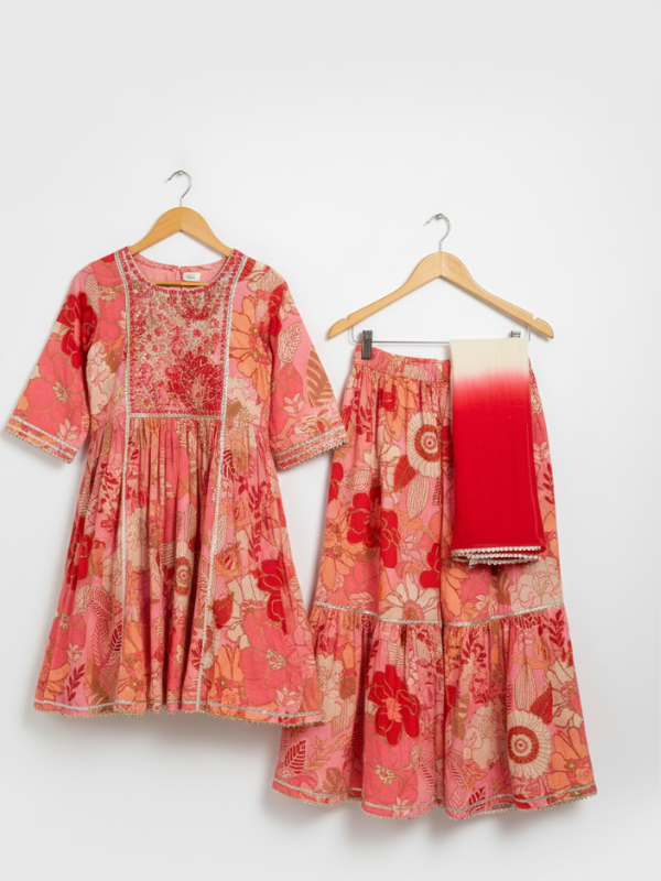 Girls' three-piece ethnic suit in a coral and peach floral print, consisting of a tiered Kurti, matching Garara, and a white-to-red ombre dupatta.