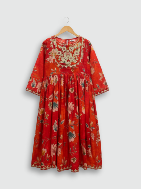 Full set laid flat: an orange/red floral-printed kurta with gold embroidered neckline, a matching tiered maxi skirt with tassels, and a printed dupatta with tassels.