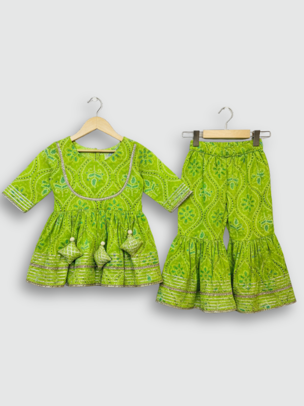 Full-length image of a young girl wearing a lime green and white floral-printed ethnic set with an embroidered peplum kurta, tiered sharara pants with a zig-zag print, and a white and green dupatta.