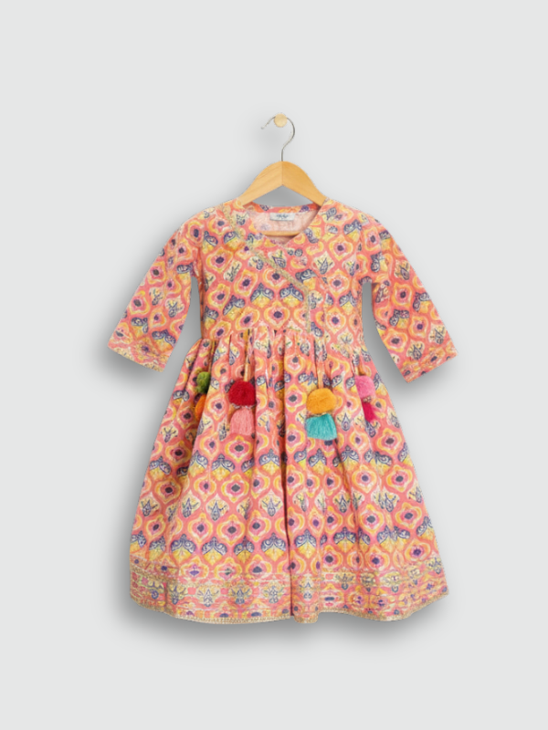 Full set laid flat: a coral pink Angrakha-style kurta with yellow/gold print and multi-colored pompoms, and matching tiered sharara pants with the same geometric print.