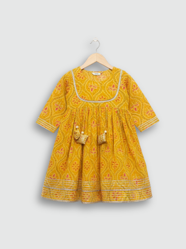 Full set laid flat: a mustard yellow Angrakha-style kurta with pink/white geometric print and multi-colored pompoms, and matching tiered sharara pants.