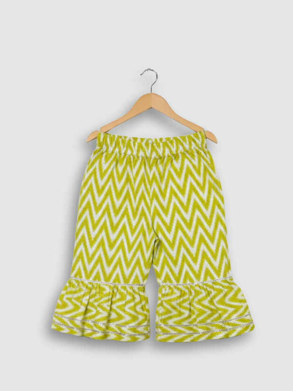 Full-length image of a young girl wearing a lime green and white floral-printed ethnic set with an embroidered peplum top, tiered gharara pants with a zig-zag print, and a white and green dupatta.