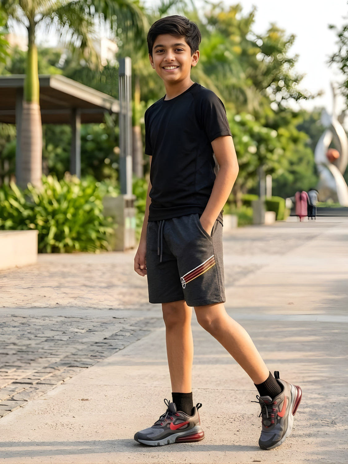 A boy standing outside wearing a black t-shirt and dark grey athletic shorts with a side stripe detail.