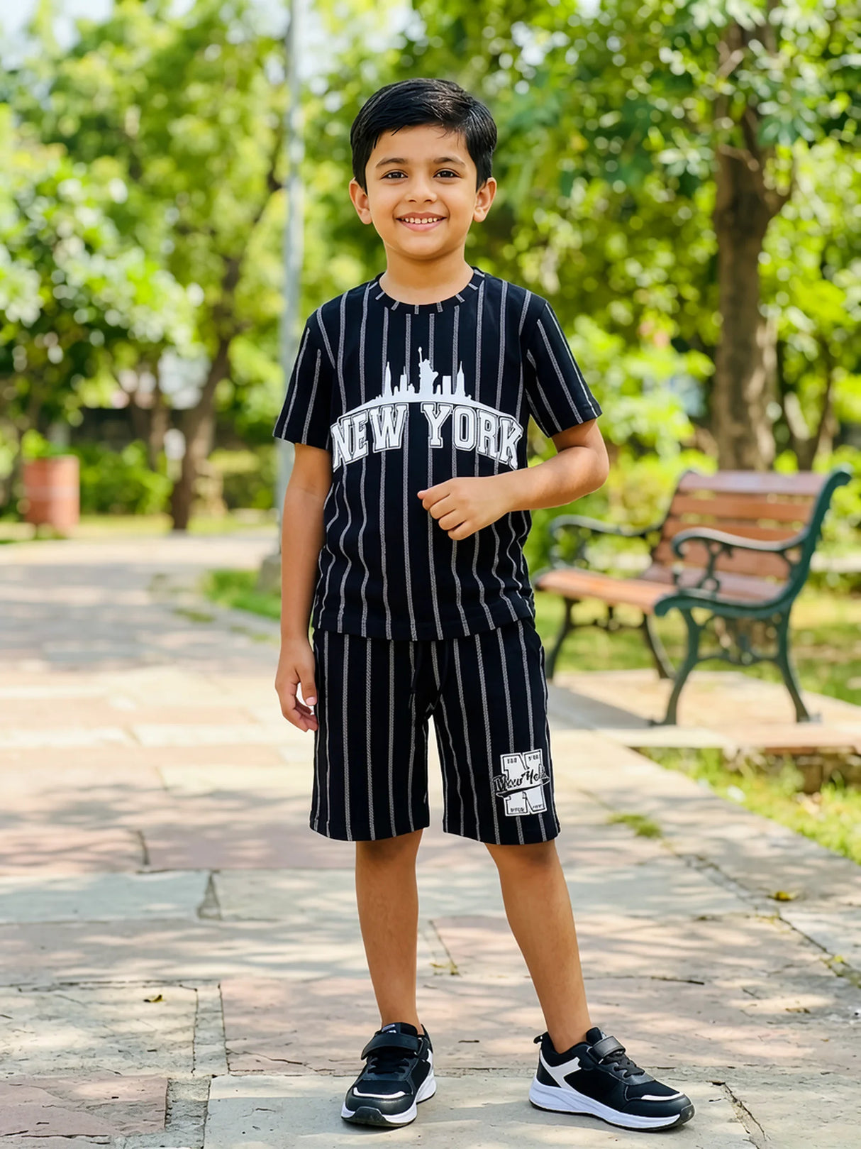Young boy wearing a black and white pinstripe co-ord set with a New York graphic print in an outdoor park setting.