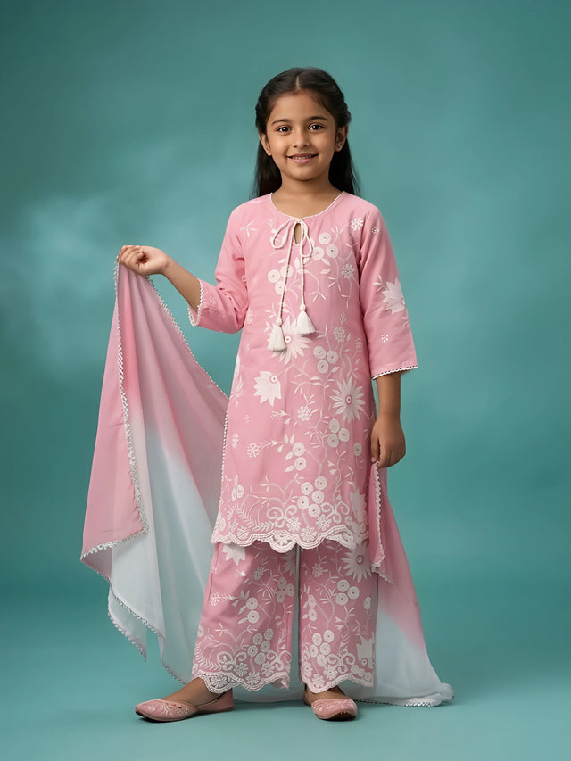 Young girl wearing a pink floral printed kurta with tassel dori, matching wide-leg palazzo pants, and an ombre white and pink dupatta.
