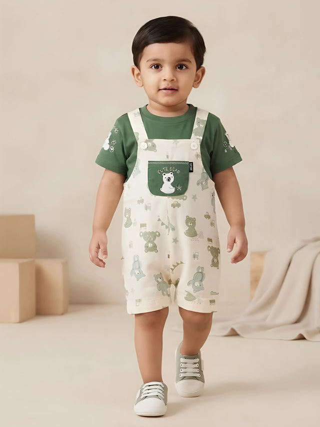 Infant boy wearing a green short-sleeve t-shirt and printed teddy bear dungaree shorts with a front patch pocket.