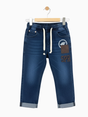 Full-length view of boys' dark wash denim jeans with a white drawstring, embroidered patches, and rolled cuffs.