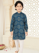 Young boy modeling a long-sleeve, teal blue Kurta with a gold bandhani print and white traditional pants in front of a decorative background.