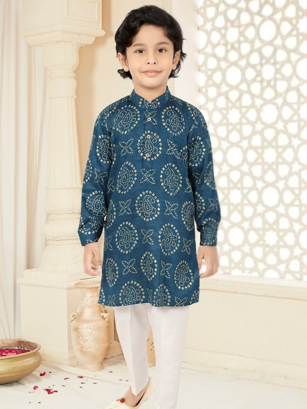 Young boy modeling a long-sleeve, teal blue Kurta with a gold bandhani print and white traditional pants in front of a decorative background.
