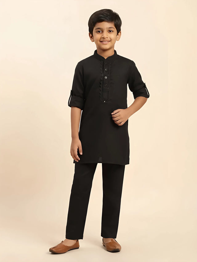 Folded black boys kurta pajama set with designer embroidered placket and matching pants.
