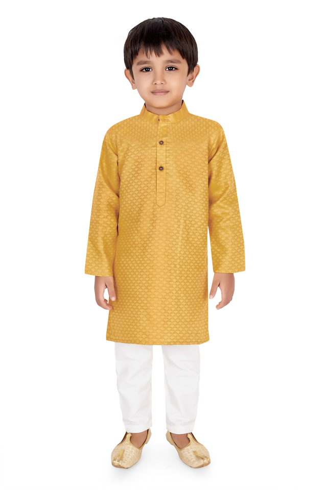 Young boy wearing a long-sleeved mustard yellow kurta with a self-woven pattern, paired with white pajama trousers and gold embroidered ethnic shoes.