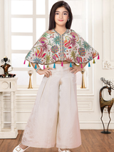 Young girl modeling a cream ethnic set with a colorful floral and paisley print cape top trimmed with tassels and textured wide-leg palazzo pants.