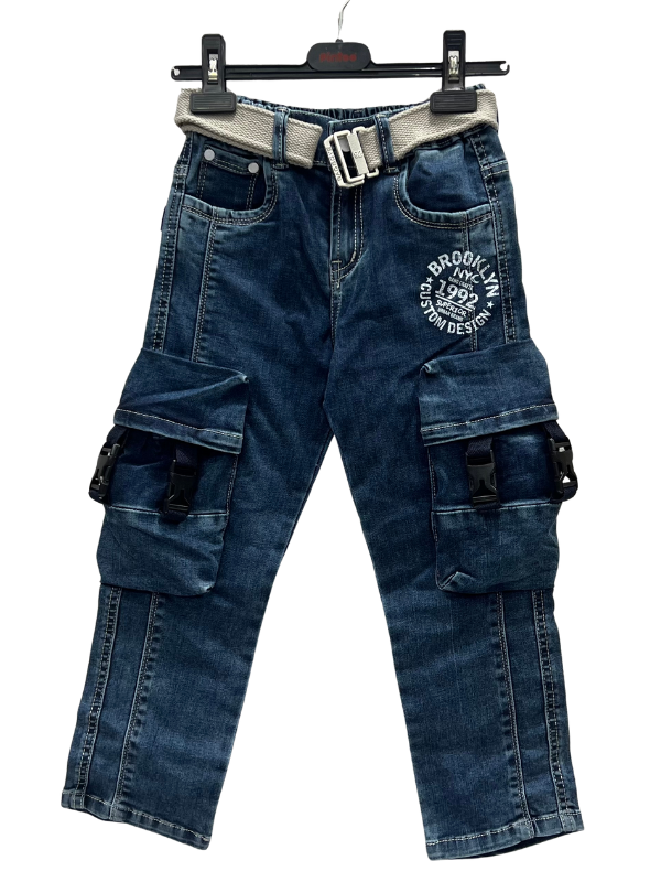 A pair of boys' dark wash denim cargo jeans hanging on a hanger, featuring large buckle-closure pockets on the legs, a white 'Brooklyn' graphic, and a light gray canvas belt.