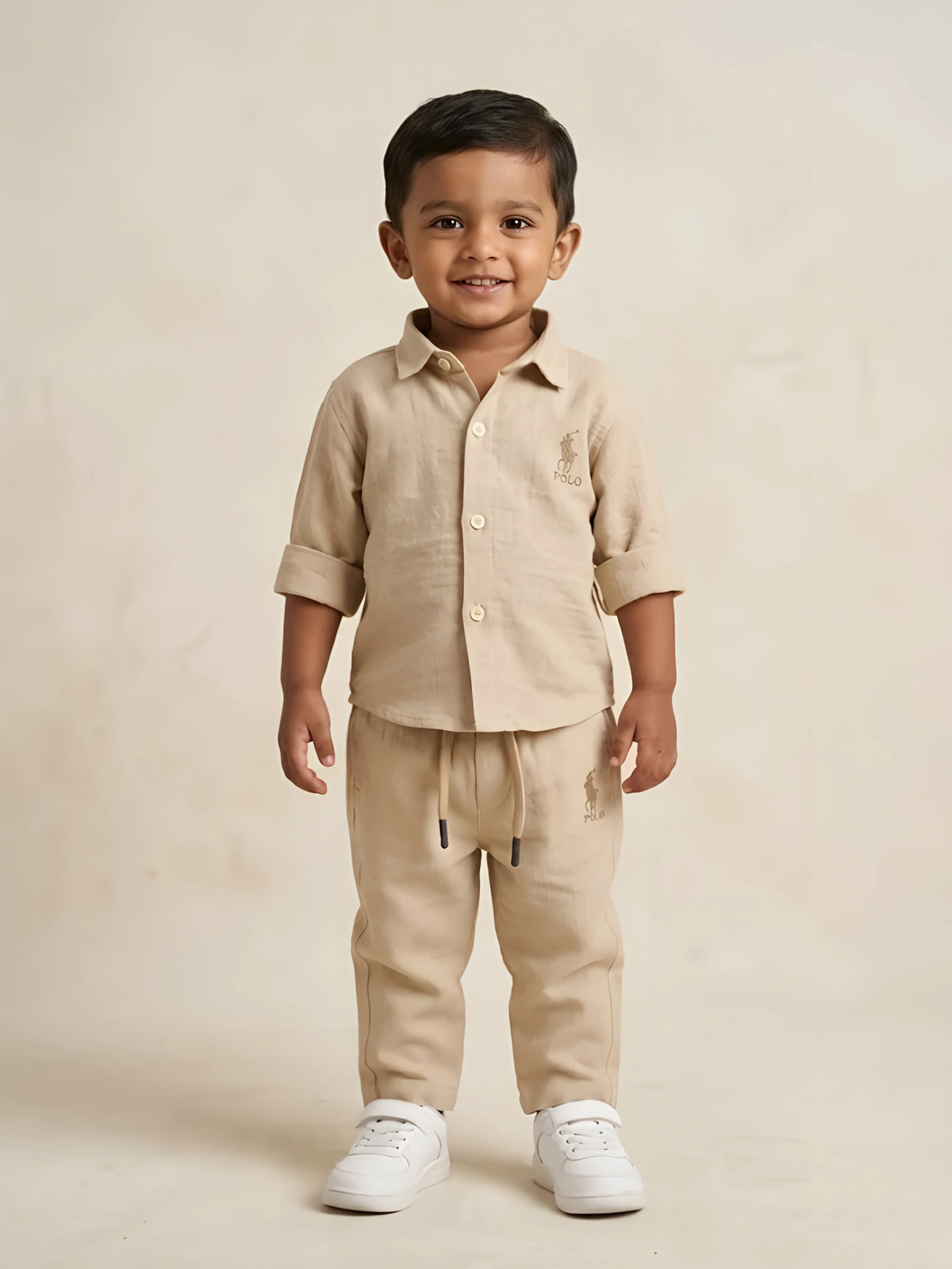Young boy wearing a stylish cream solid two-piece shirt and drawstring trousers co-ord set with white sneakers.