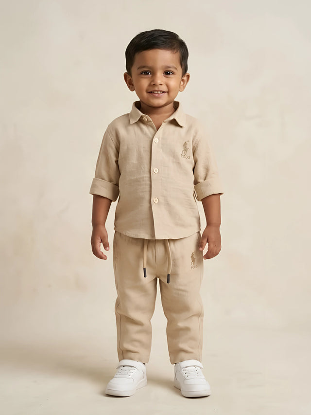 Young boy wearing a stylish cream solid two-piece shirt and drawstring trousers co-ord set with white sneakers.