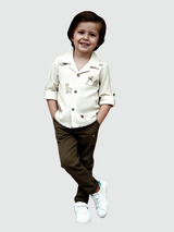 Young boy smiling in a cream embroidered shirt with a Revere collar and dark olive green trousers. The smart-casual set is completed with white sneakers