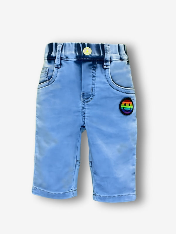 Boys' light blue denim or twill pants with an elastic waist, straight leg, and a colorful rainbow smiley face embroidered patch on the right thigh.