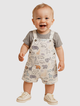 Happy baby wearing a cream/light gray overall romper with a neutral colored safari animal pattern, styled over a plain gray short-sleeve t-shirt.