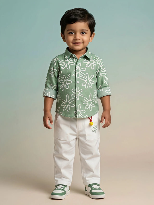 Young boy wearing a sage green floral printed shirt with rolled-up sleeves and white utility trousers.