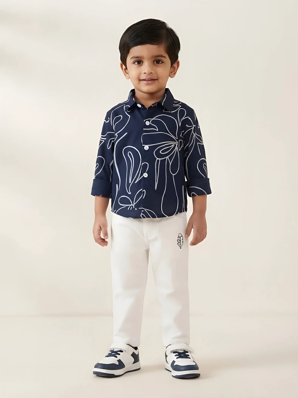 Young boy wearing a navy blue full sleeve abstract print shirt with white trousers and sneakers
