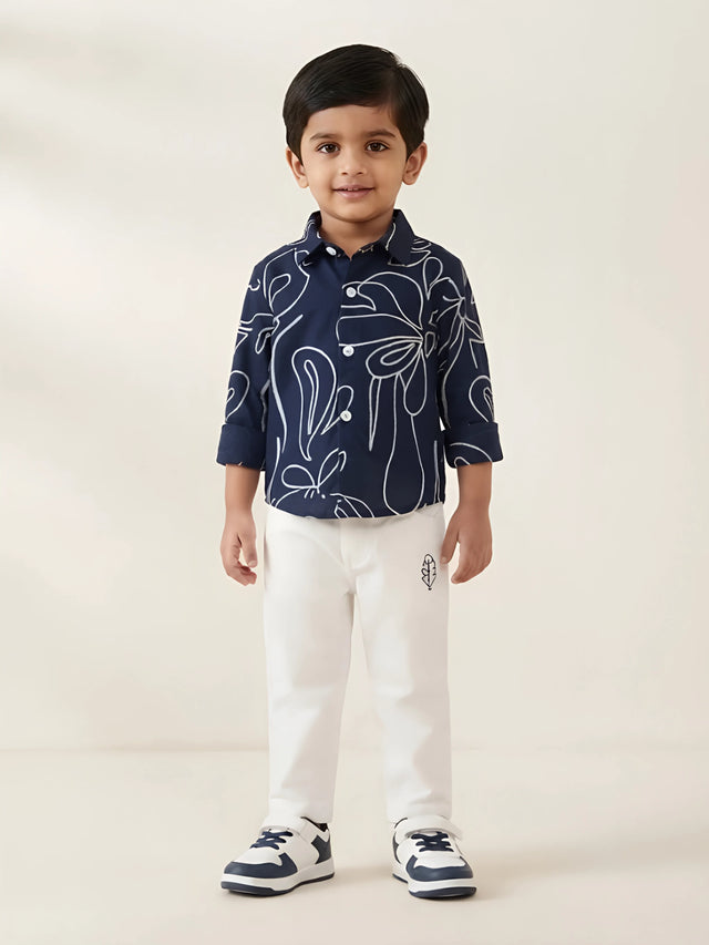 Young boy wearing a navy blue full sleeve abstract print shirt with white trousers and sneakers