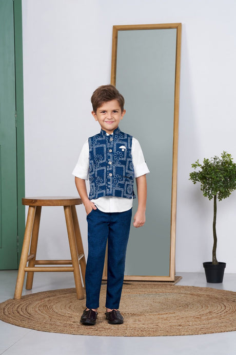 Young boy smiling in a blue Bandhani print ethnic waistcoat, white short-sleeve shirt, and matching blue tailored trousers. Full-length product shot for a boy's festive suit set.