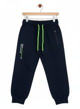 A pair of boys' navy blue fleece jogger track pants with an elastic waist, bright neon green contrast drawstring, ribbed ankle cuffs, and a vertical zippered pocket.