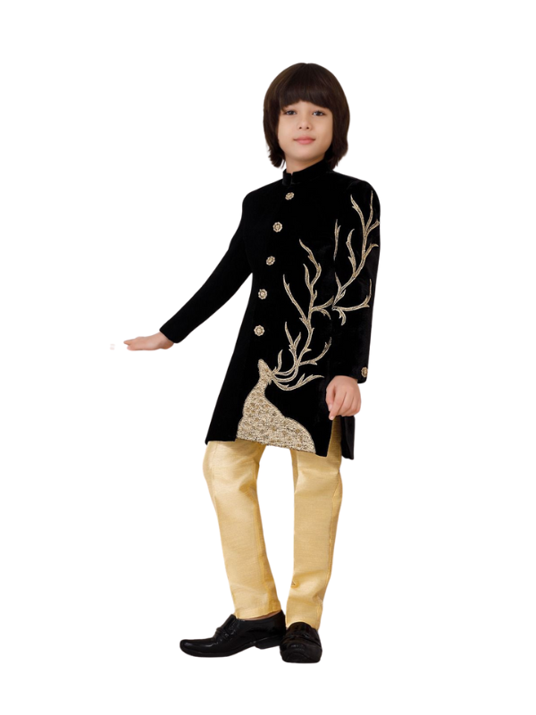 Young boy wearing an elegant black velvet sherwani jacket with detailed gold zari work featuring a deer and tree motif on the side, paired with contrasting shiny gold silk trousers.