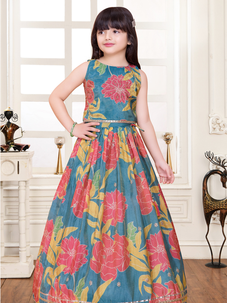 Young girl wearing a sleeveless lehenga choli set in a teal blue fabric featuring large, bright pink and yellow floral prints, with a gold trim at the waist.