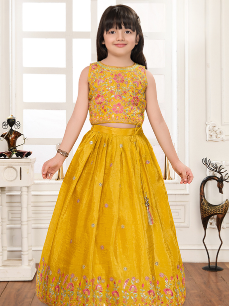 Young girl wearing a sleeveless, heavily embroidered mustard yellow lehenga choli set with pink and green floral embroidery on the top and skirt border, ideal for Haldi functions.