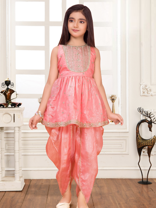 Young girl modeling a sleeveless peach/pink ethnic wear set with a short, flared peplum Kurti top and draped dhoti-style pants.