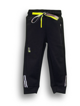 Close-up view of a pair of solid black fleece boys' track pants/joggers with a wide elastic waistband, cuffed ankles, and a small pink vertical graphic on the lower leg.