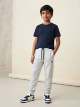 Young boy wearing light grey casual trackpants with an elastic drawstring waist and side pockets paired with a navy blue t-shirt